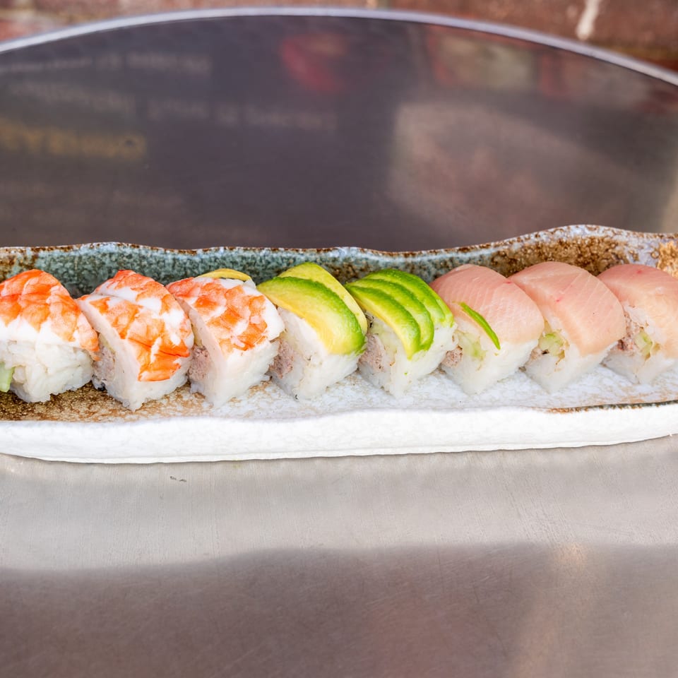 A row of What the Fish Sushi rolls with shrimp, avocado, and tuna on a decorative plate.