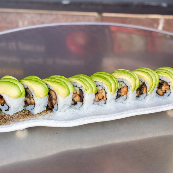 A row of What the Fish Sushi's avocado-topped sushi rolls with eel and cucumber on a white plate.