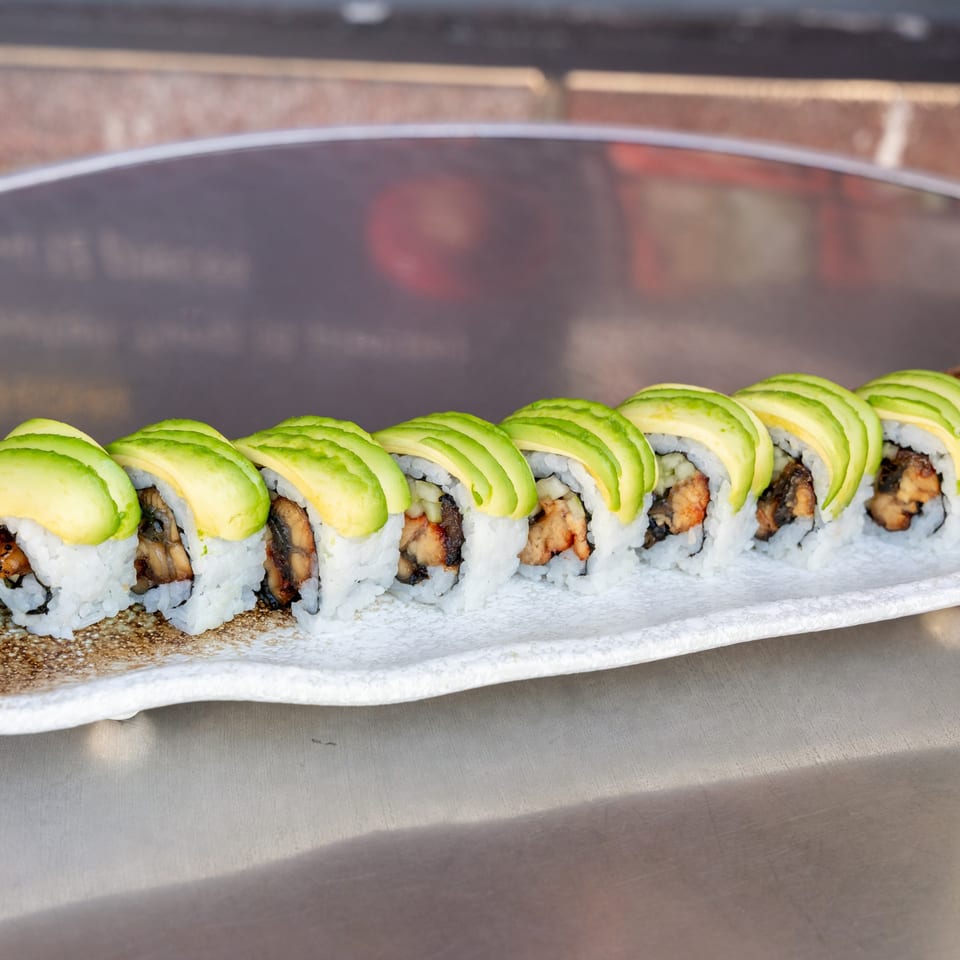 A row of What the Fish Sushi's avocado-topped sushi rolls with eel and cucumber on a white plate.