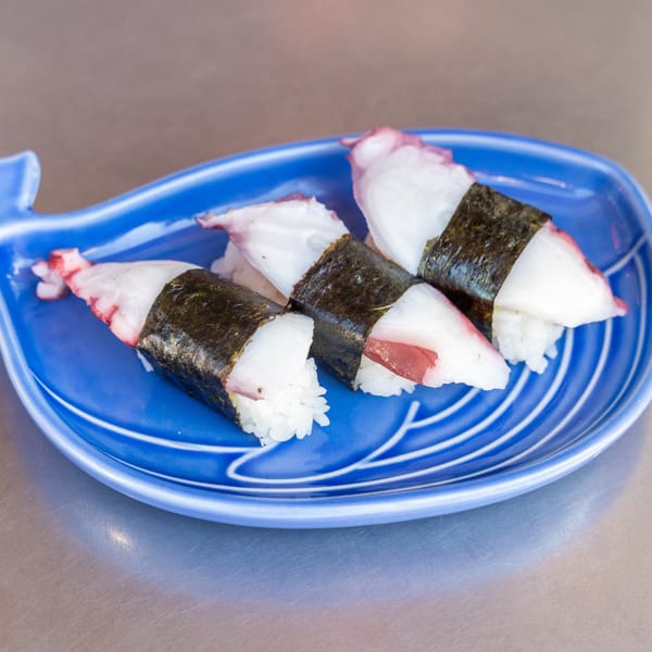 Three octopus nigiri sushi pieces with nori on a blue whale-shaped plate.