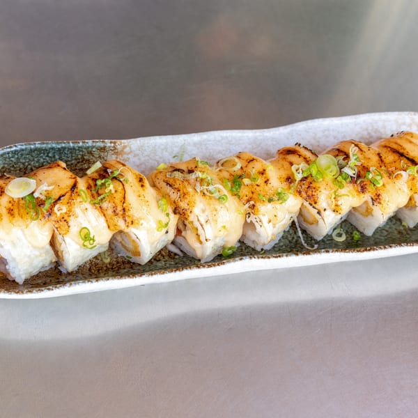 A row of What the Fish Sushi's baked scallop rolls, topped with creamy sauce and green onions.