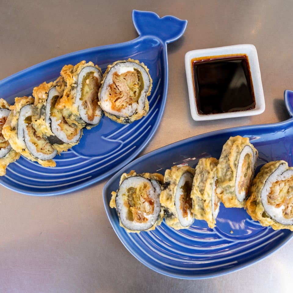 Two blue whale-shaped plates hold crispy fried sushi rolls with a side of soy sauce.