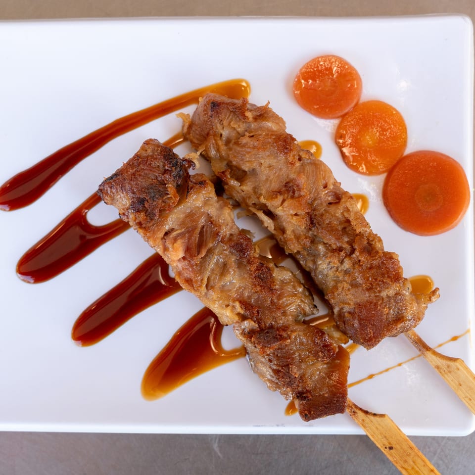 Two skewers of grilled meat with sauce and three carrot slices on a white plate.