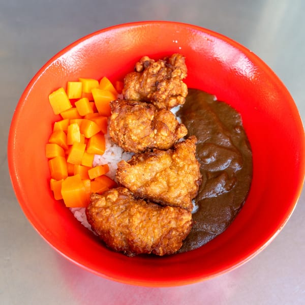 A red bowl of What the Fish Sushi's fried chicken, rice, curry, and diced mango.